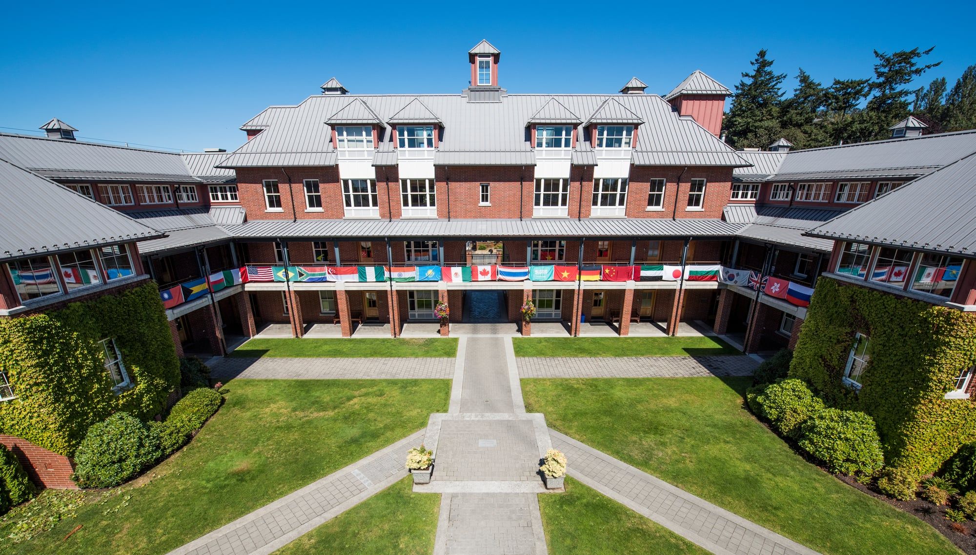 Vista aérea del patio de un boarding school canadiense de ladrillo rojo con banderas internacionales.