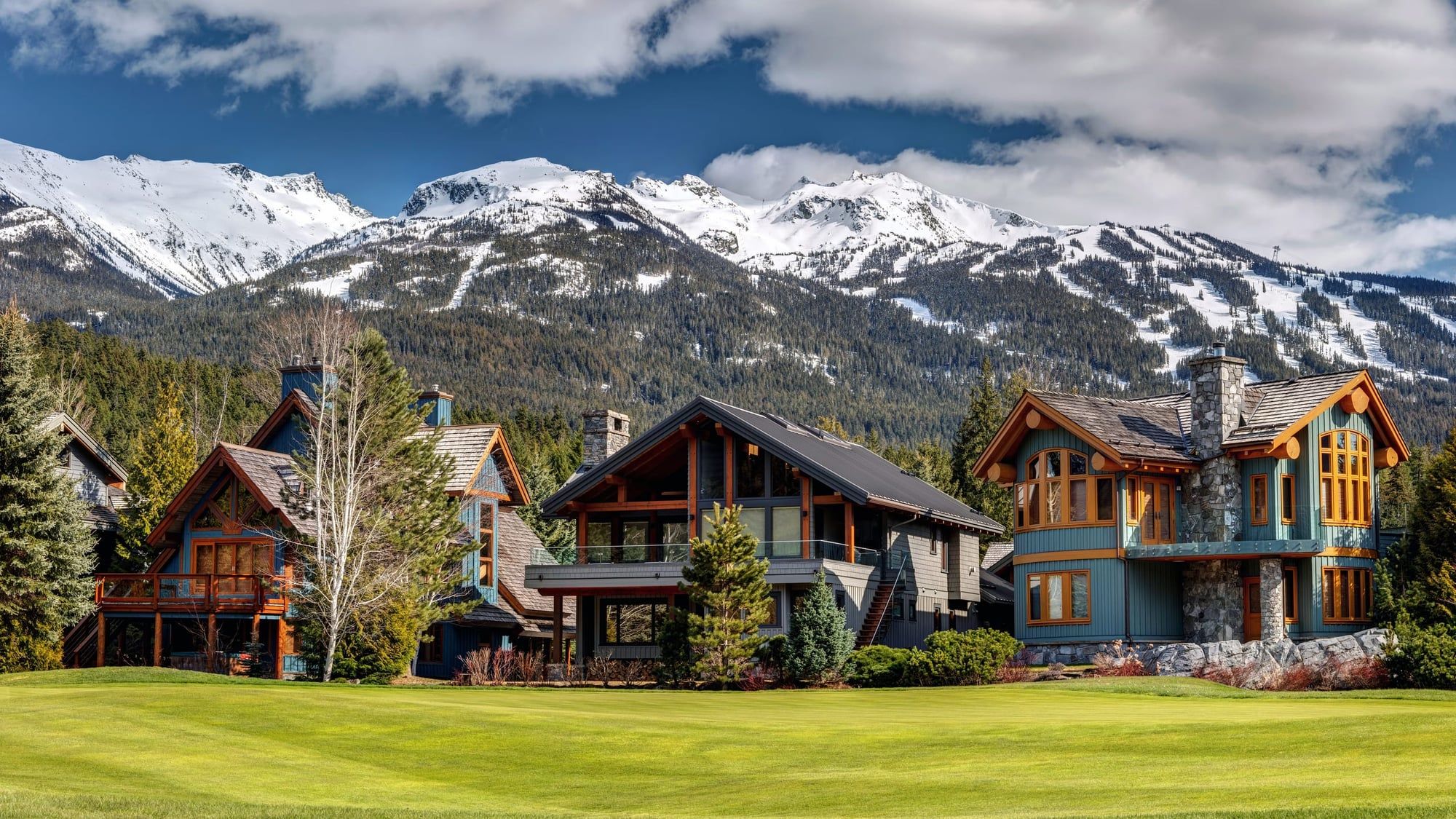 Casas de madera y piedra sobre un césped, con las montañas nevadas de Whistler al fondo.